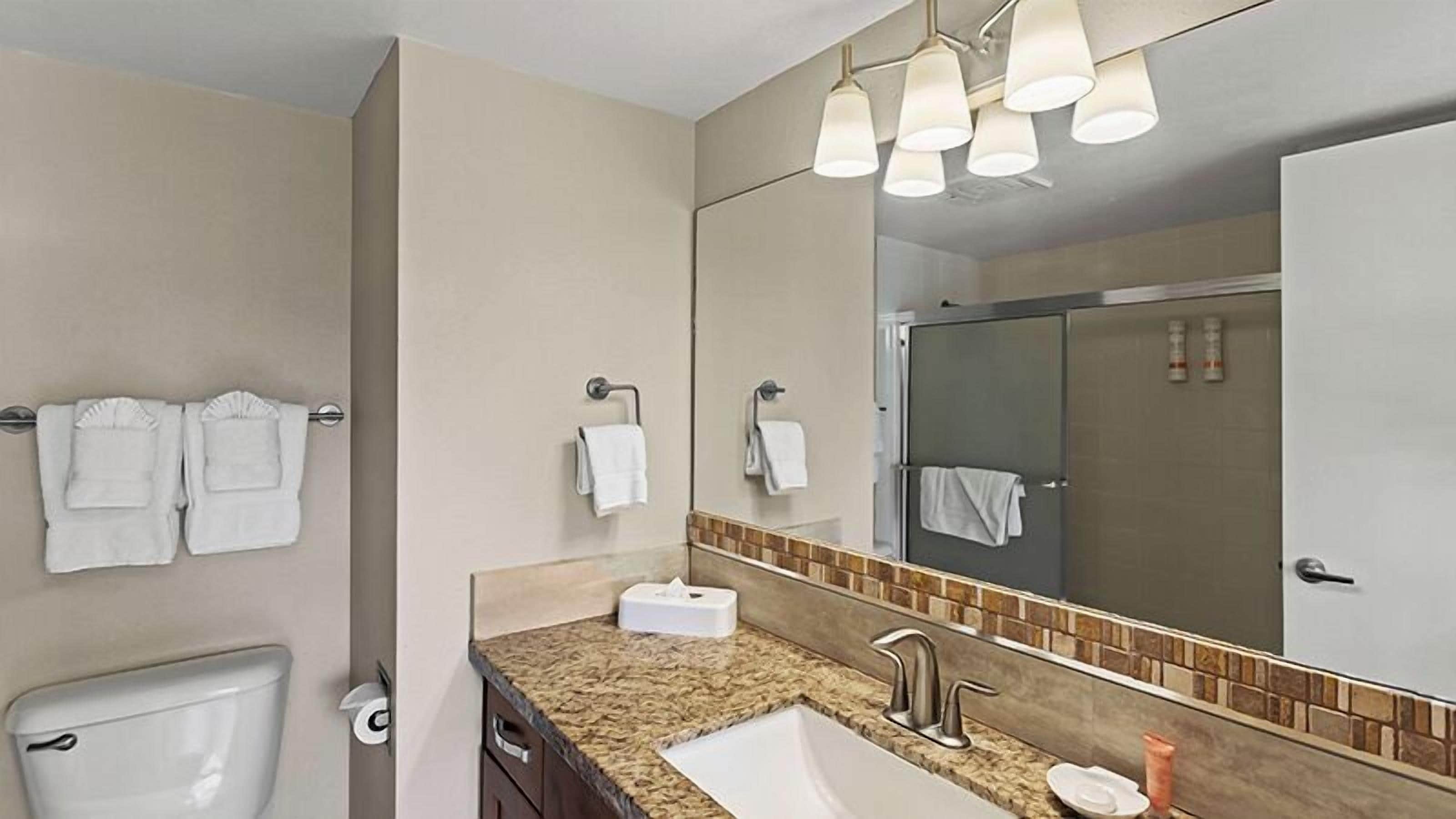 Un bagno con il water, un lavandino e uno specchio. Asciugamani appesi al muro.