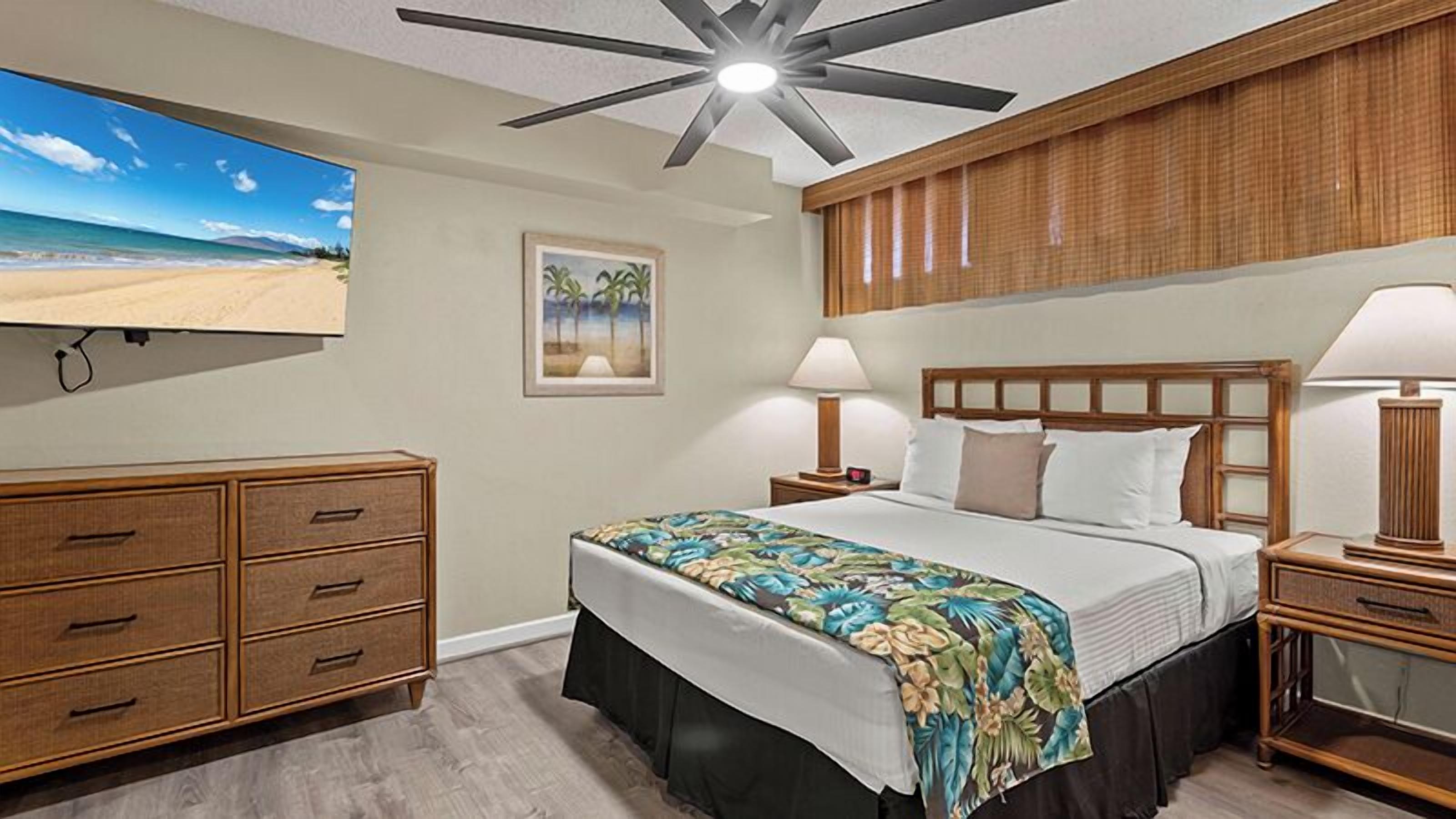 Habitación de hotel con cama, lámparas de noche, televisor, cómoda de madera y ventilador de techo.
