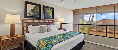 Habitación de hotel con cama, dos mesitas de noche con lámparas, ventilador de techo y un ventanal con vistas.