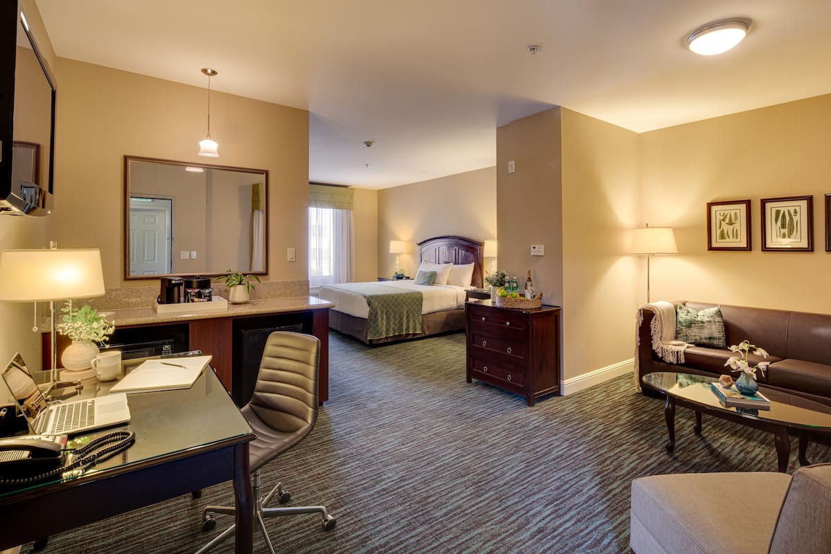 Habitación de hotel con escritorio, silla, cama y zona de estar con sofá y mesa de centro.