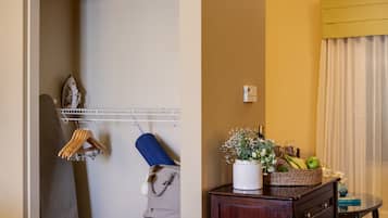 A hotel room with a wardrobe, a desk with a vase of flowers, and a small table with a book and a glass.