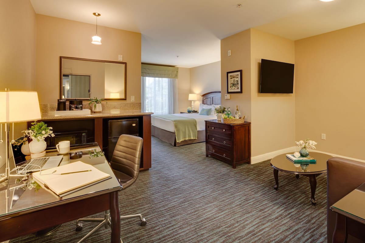 Habitación de hotel con escritorio, silla, cama, cómoda y televisor en la pared.
