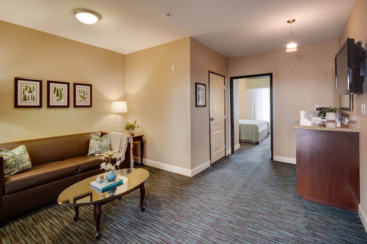 Habitación de hotel con sala de estar que incluye un sofá, una mesa de centro e impresiones botánicas enmarcadas en la pared.