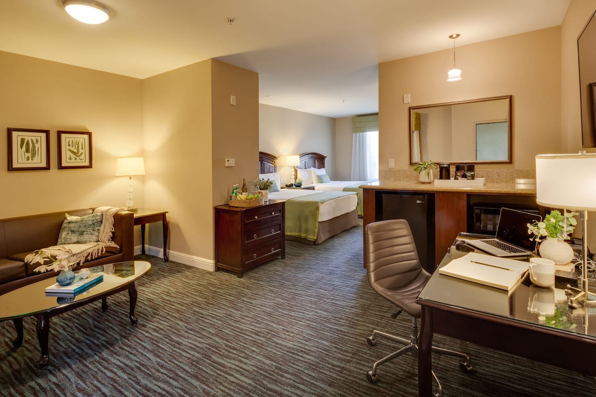 Una habitación de hotel con cama, escritorio con computadora portátil, silla, sofá, mesa de centro y lámpara.