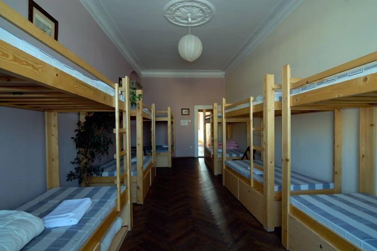 A dormitory room with bunk beds, wooden beams, a herringbone floor, and a ceiling fan.