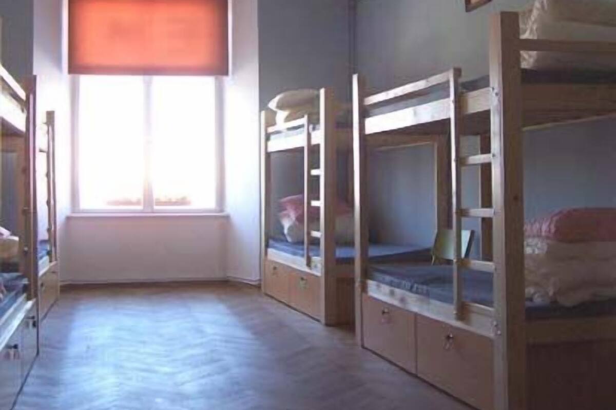 A room with bunk beds, a window with blinds, a ceiling fan, and a light fixture.