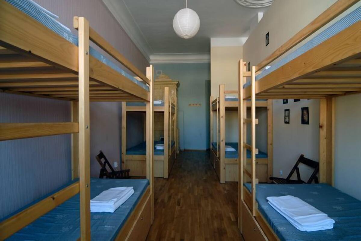 A dormitory room with bunk beds, a wooden floor, and a white ceiling light.