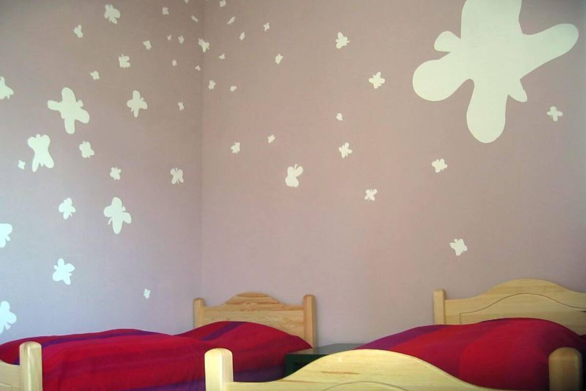 A bedroom with two wooden beds, each with a red and purple bedspread. The walls are decorated with white butterfly decals.