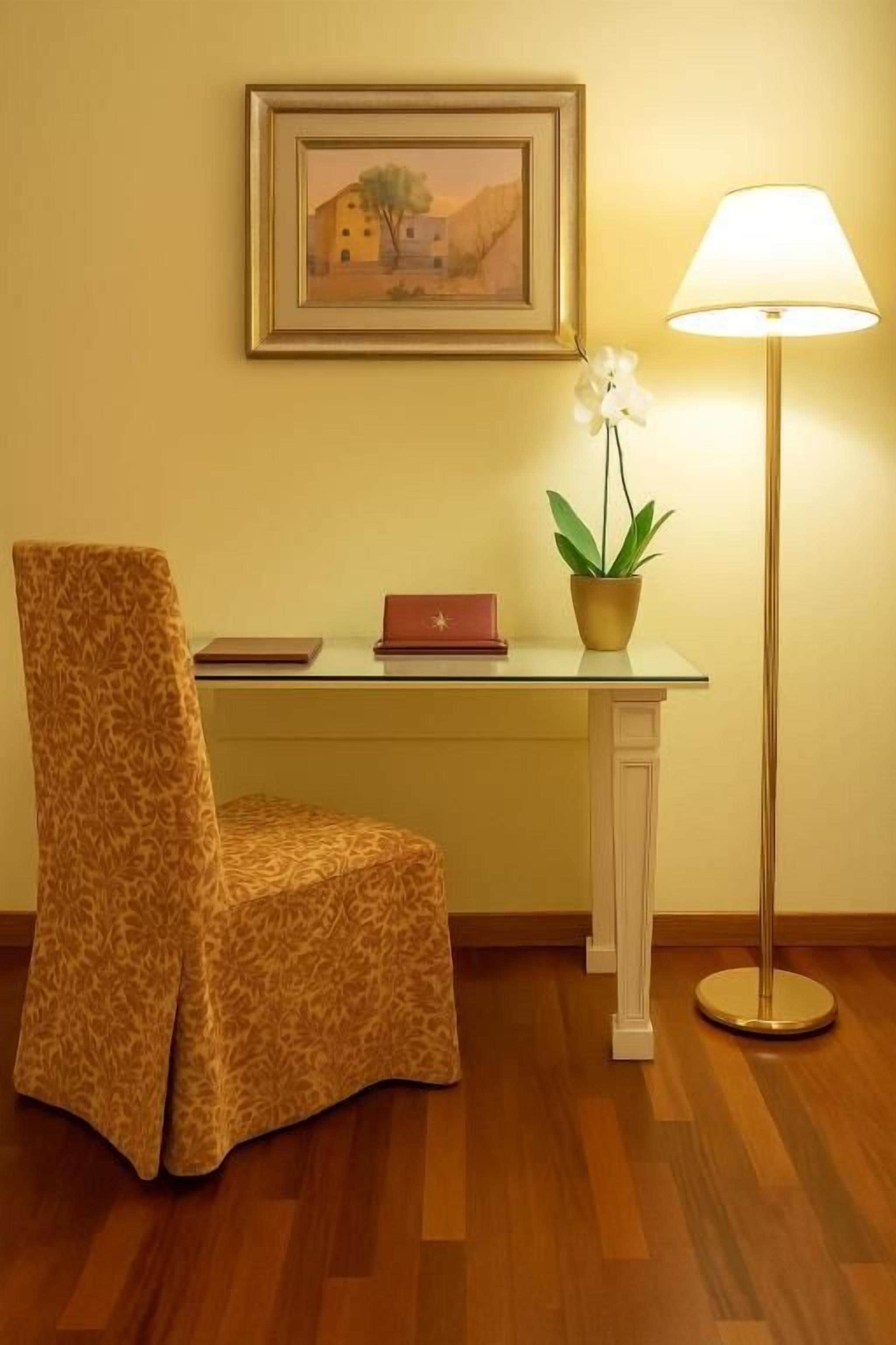 Una silla, un escritorio con una lámpara, un cuadro enmarcado y una planta en maceta.