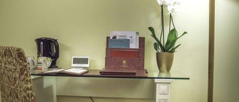 A room with a desk, chair, lamp, and a framed picture on the wall.