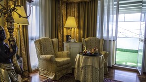 Una habitación con dos sillones, una mesita con una bandeja de aperitivos, una lámpara y una estatua.