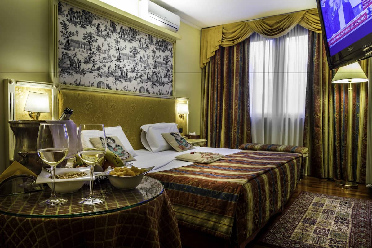 A hotel room with a bed, two bedside tables, a television, and a wall with a patterned wallpaper.