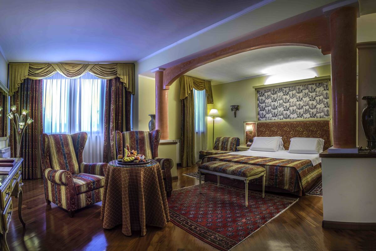 A hotel room with a large bed, a smaller bed, a desk, a chair, and a dining table.