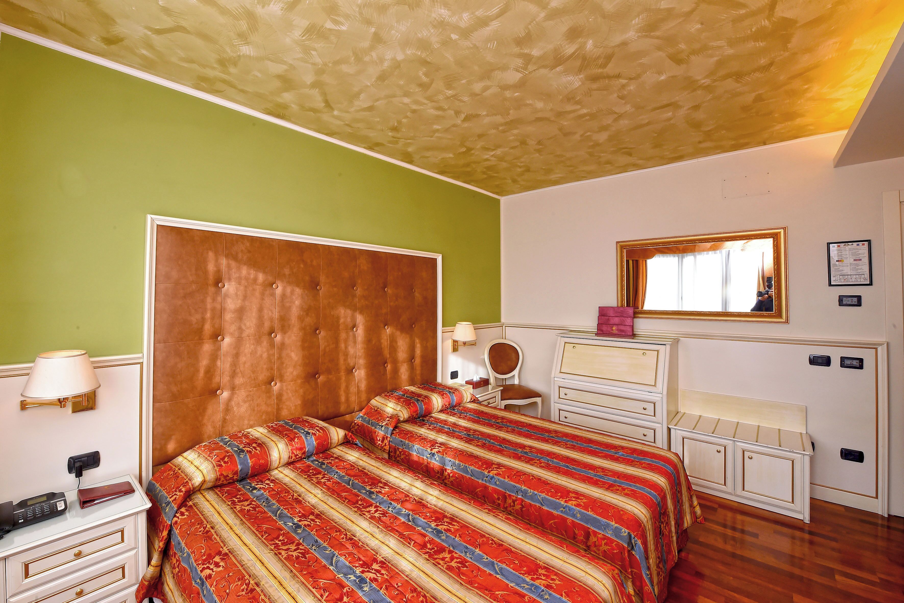 Ein Hotelzimmer mit einem großen Bett, einem Schminktisch mit Spiegel und einem Schreibtisch mit Lampe.