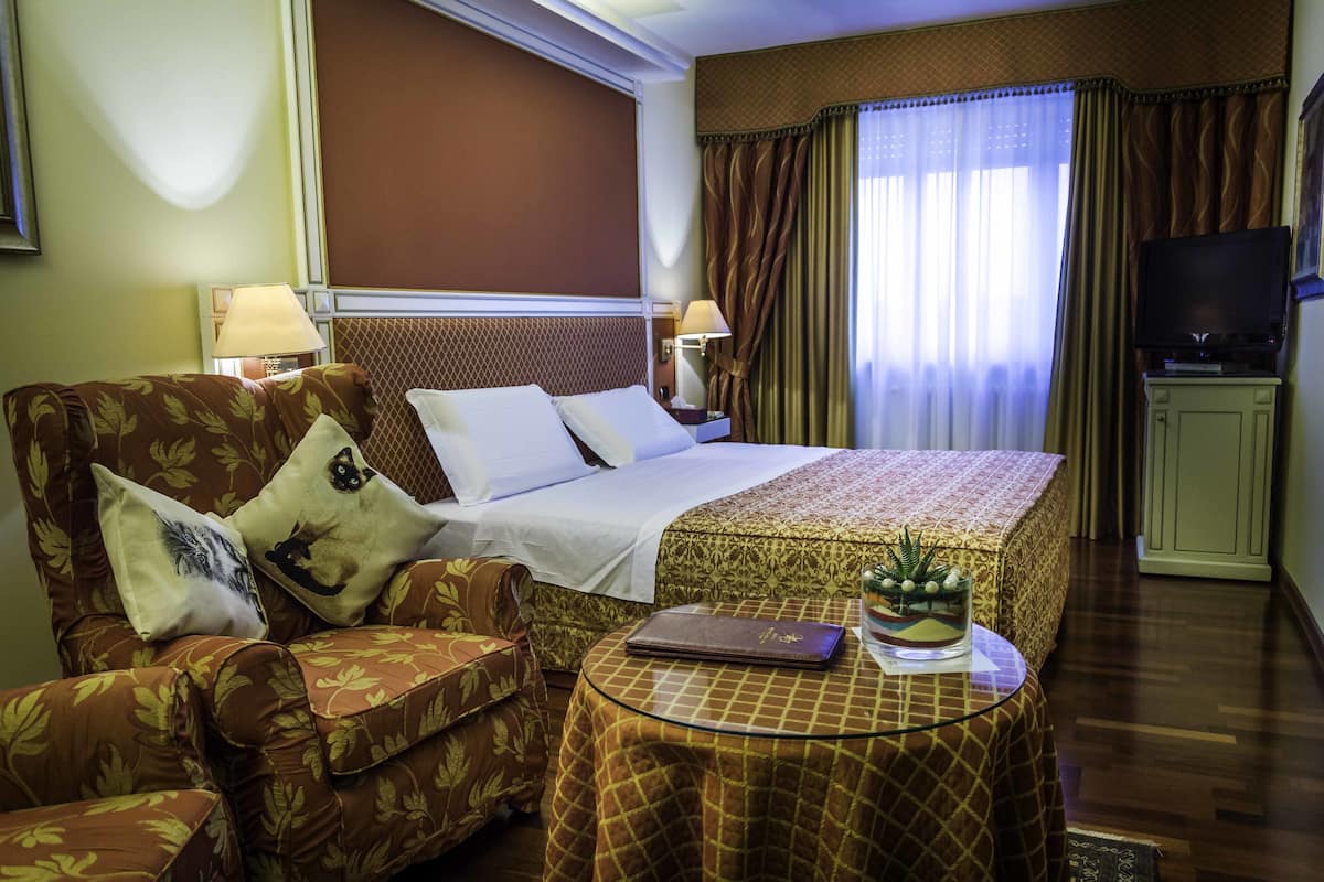 A hotel room with a bed, a sofa, a small table with a laptop, and a television.