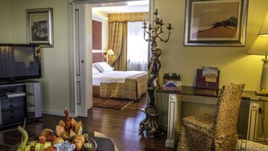 Habitación de hotel con cama, televisión, mesa de comedor con fruta, un candelabro decorativo y un sillón con estampado.