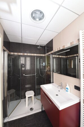A modern bathroom with a glass-enclosed shower, a white sink, and a red vanity.