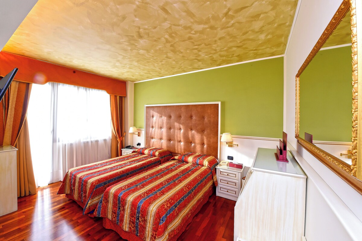 A hotel room with a large bed, a dresser, a mirror, and a window with curtains.