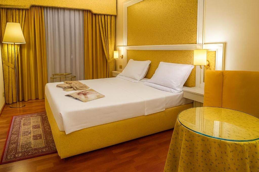 Une chambre d’hôtel avec un lit, des lampes de chevet, une petite table et une fenêtre avec des rideaux.