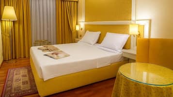 A hotel room with a bed, bedside lamps, a small table, and a window with curtains.