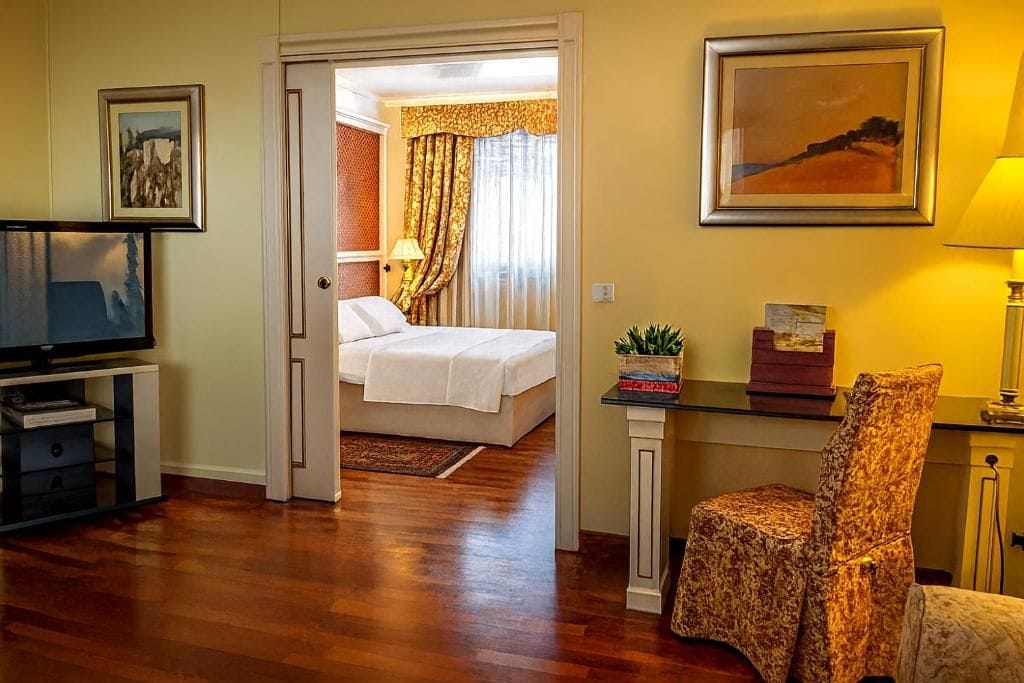 A hotel room with a bed, a television, a desk with a lamp, and a chair.
