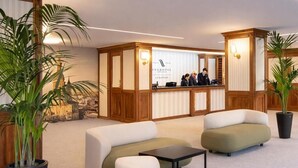 Un área de recepción con mostrador, dos sofás, una mesita y plantas en macetas.