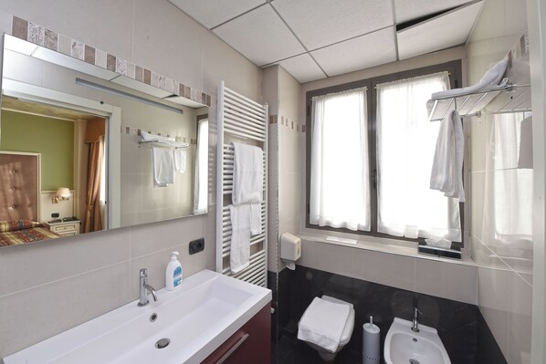 Un baño moderno con un espejo grande, dos lavamanos, un perchero para toallas y una ventana con cortinas.