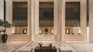 Un hall espacioso con una mesa de recepción, dos orquídeas en macetas, una mesa baja de café oscura y un sofá color crema.