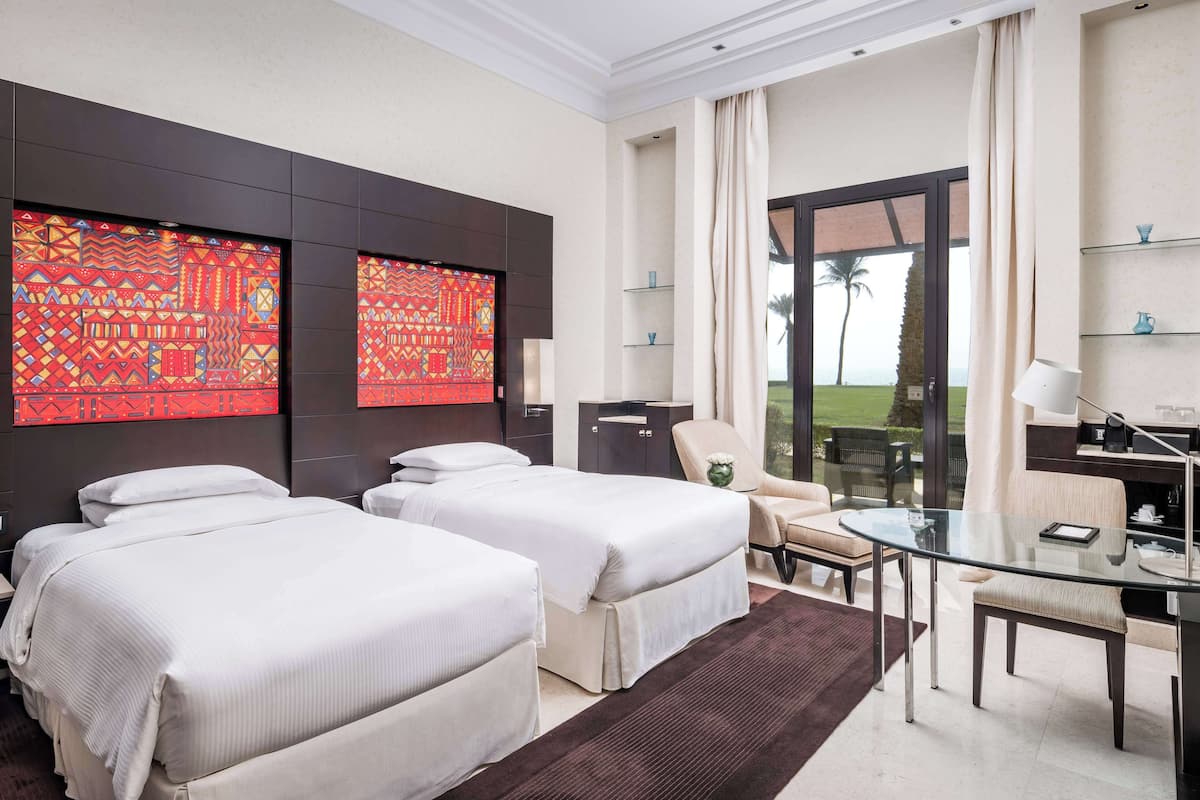 Une chambre d’hôtel avec deux lits, une table en verre, une chaise et une vue sur l’extérieur.