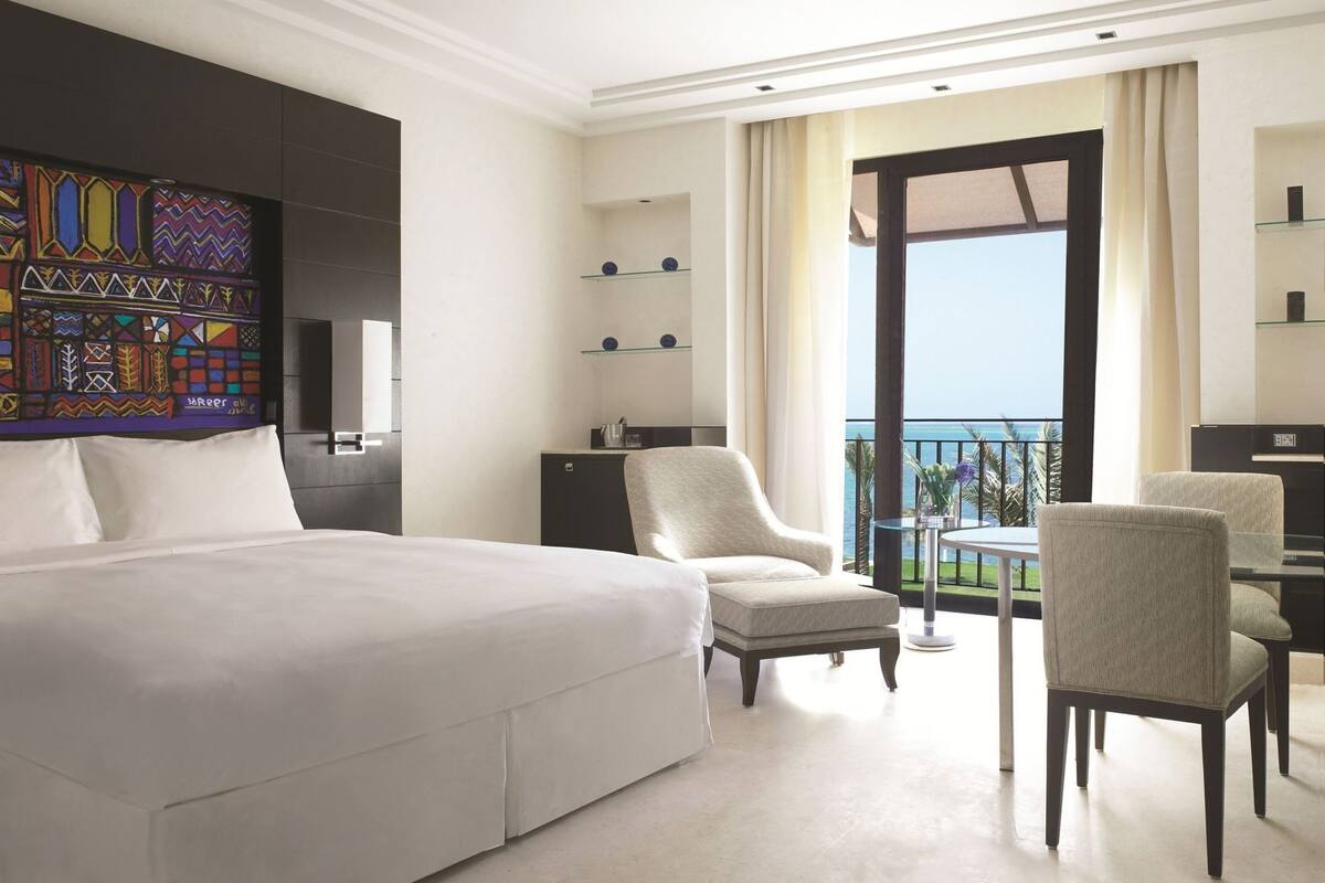 Une chambre d’hôtel avec un grand lit, une chaise, une petite table, une télévision et un balcon avec vue.