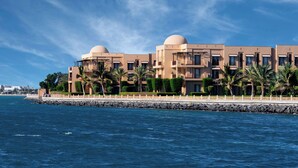 Un hotel moderno con varios pisos, vista al agua y palmeras.