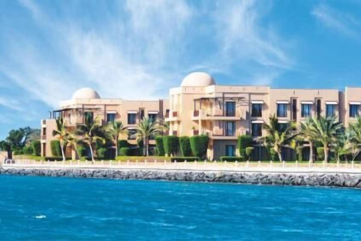 Un hôtel situé sur la côte, composé de plusieurs bâtiments, bordé de palmiers et offrant une vue sur un ciel bleu azur.