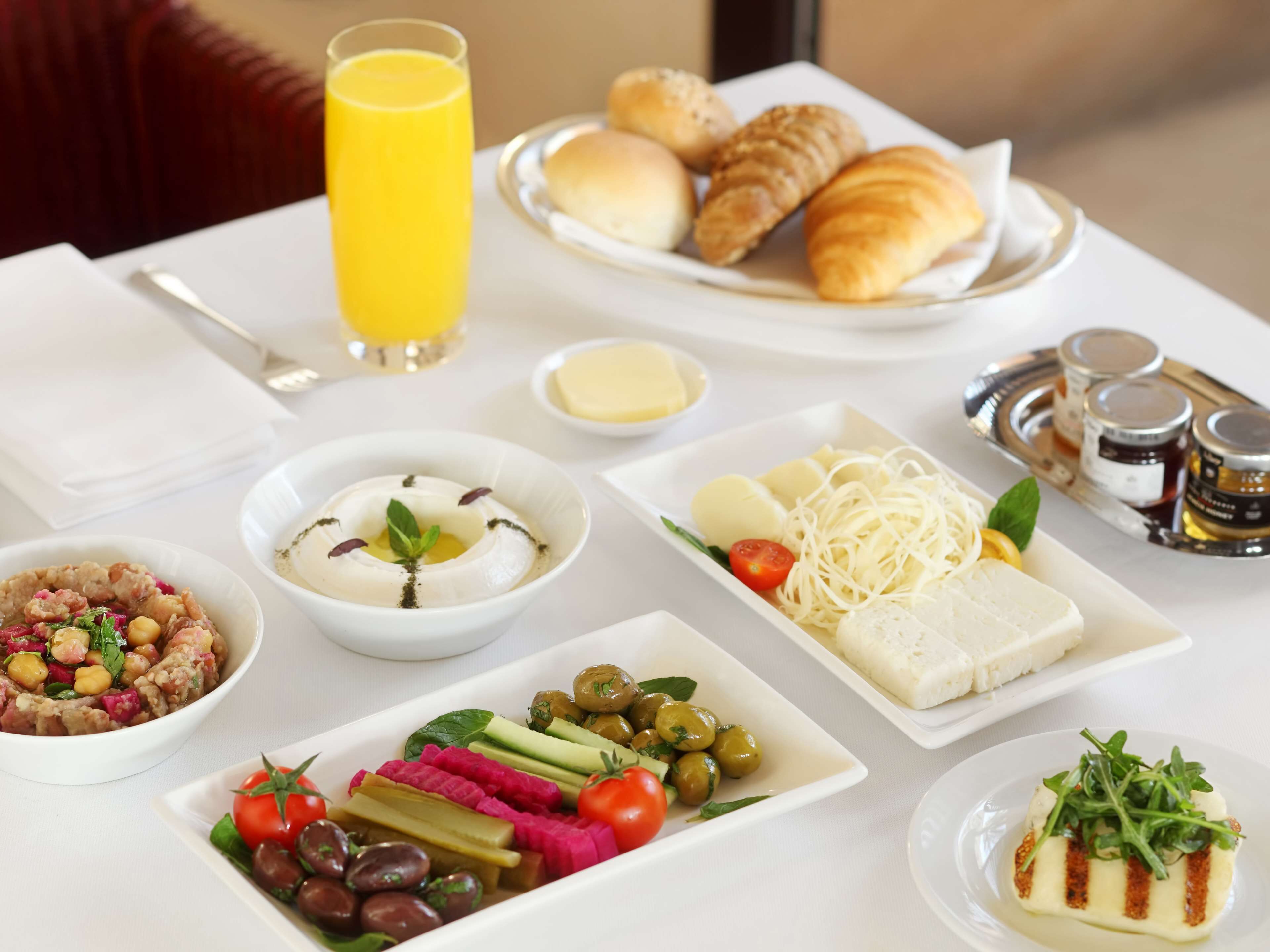 Una mesa de desayuno con diversos platos, incluyendo cruasanes, un vaso de zumo de naranja, y una variedad de ensaladas y quesos.