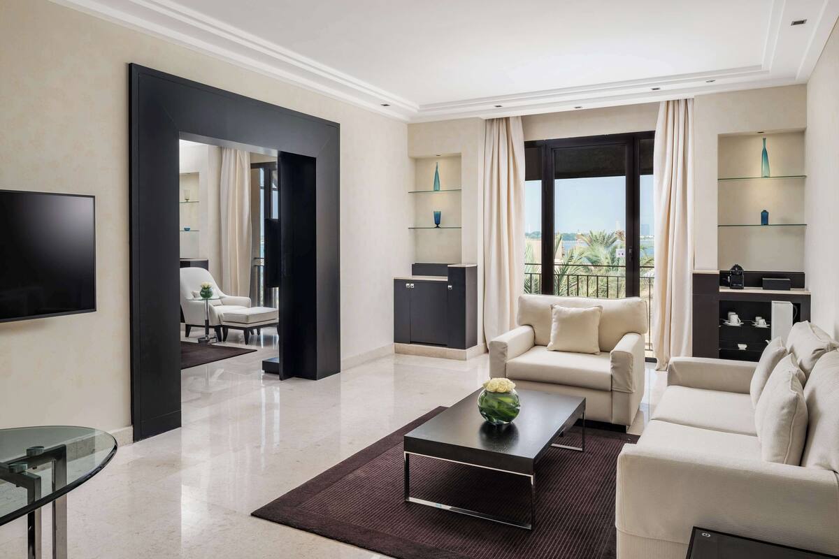 Un salon moderne avec un canapé, une table basse et un téléviseur. Il y a un balcon d’où l’on peut admirer des palmiers.