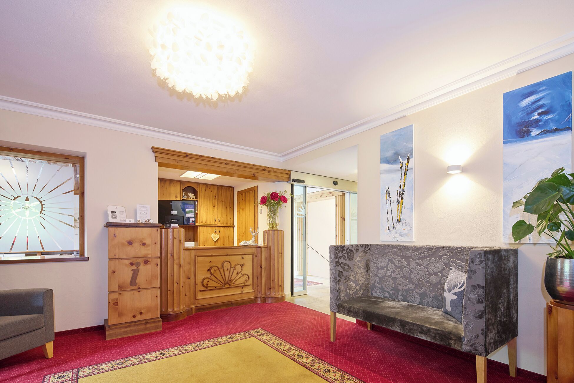A hotel lobby with a wooden reception desk, a sofa, a red carpet, and wall art.