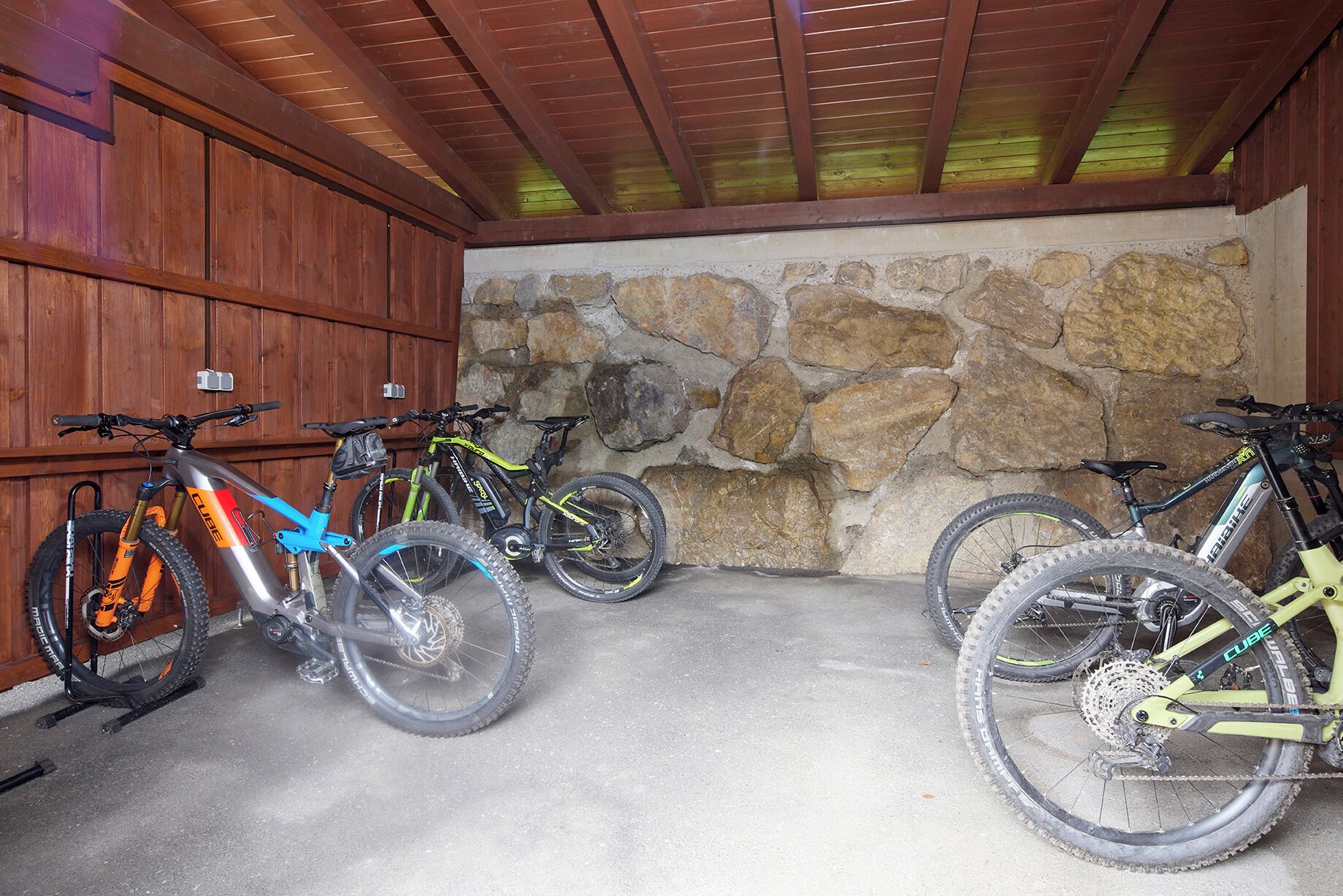 Un espace de stationnement pour vélos abrité, doté d’un mur en pierre et d’un lambris en bois.