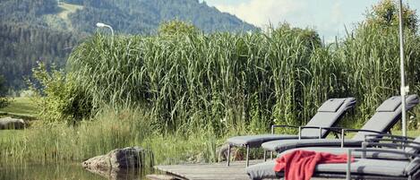 A lakeside deck with lounge chairs and an umbrella, overlooking a calm lake and dense vegetation.