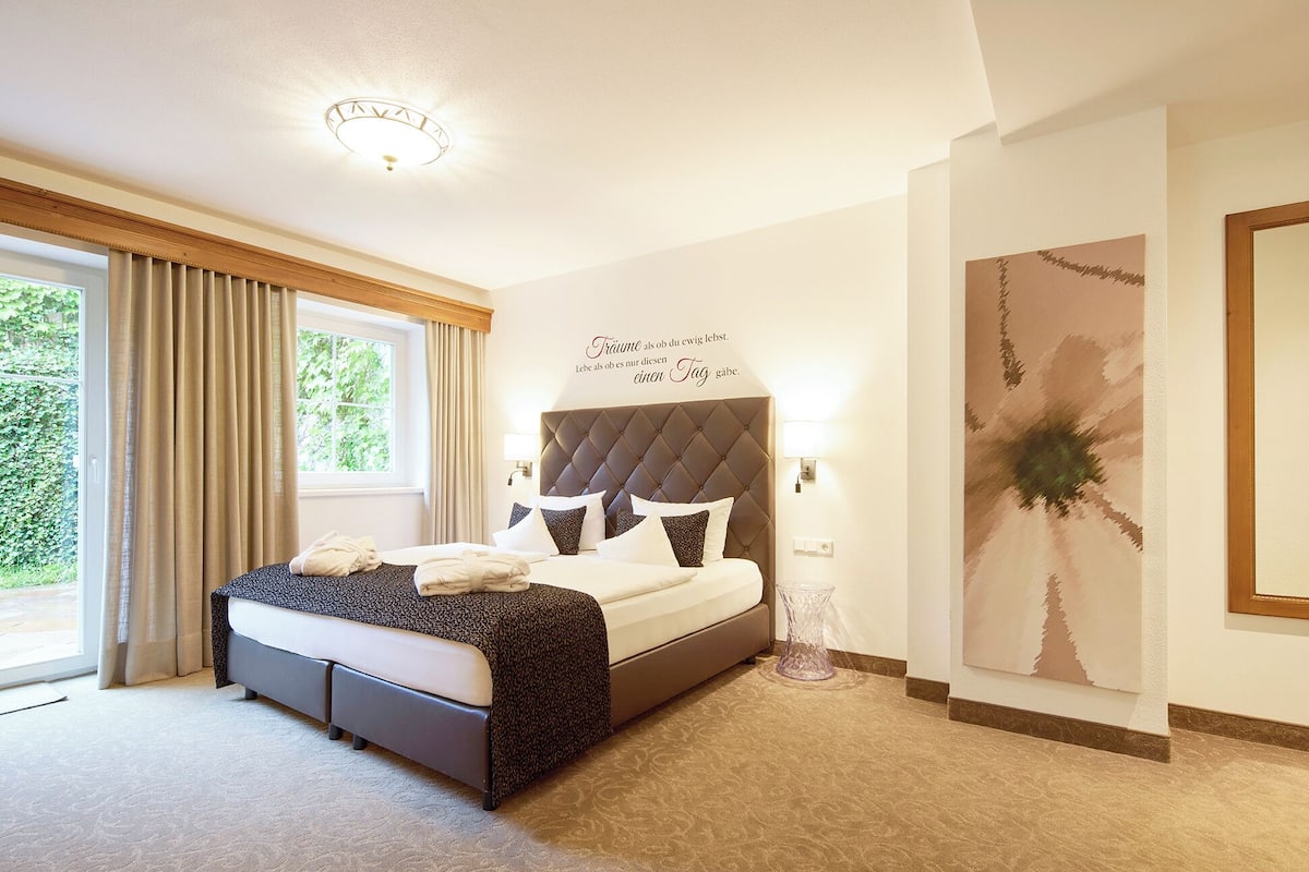 Un dormitorio con una cama grande, una ventana con cortinas, una lámpara de pared y una obra de arte abstracta.