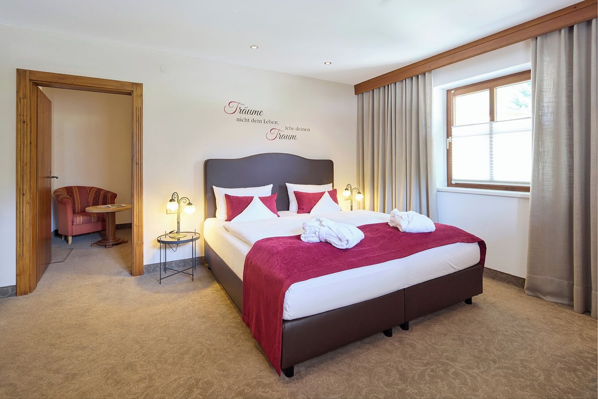 Una habitación de hotel con una cama grande, dos lámparas de noche, una manta roja y un adorno en la pared.