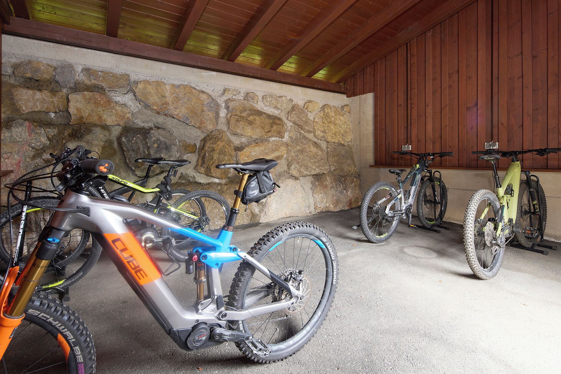 A covered bike parking area with stone walls and wooden beams.