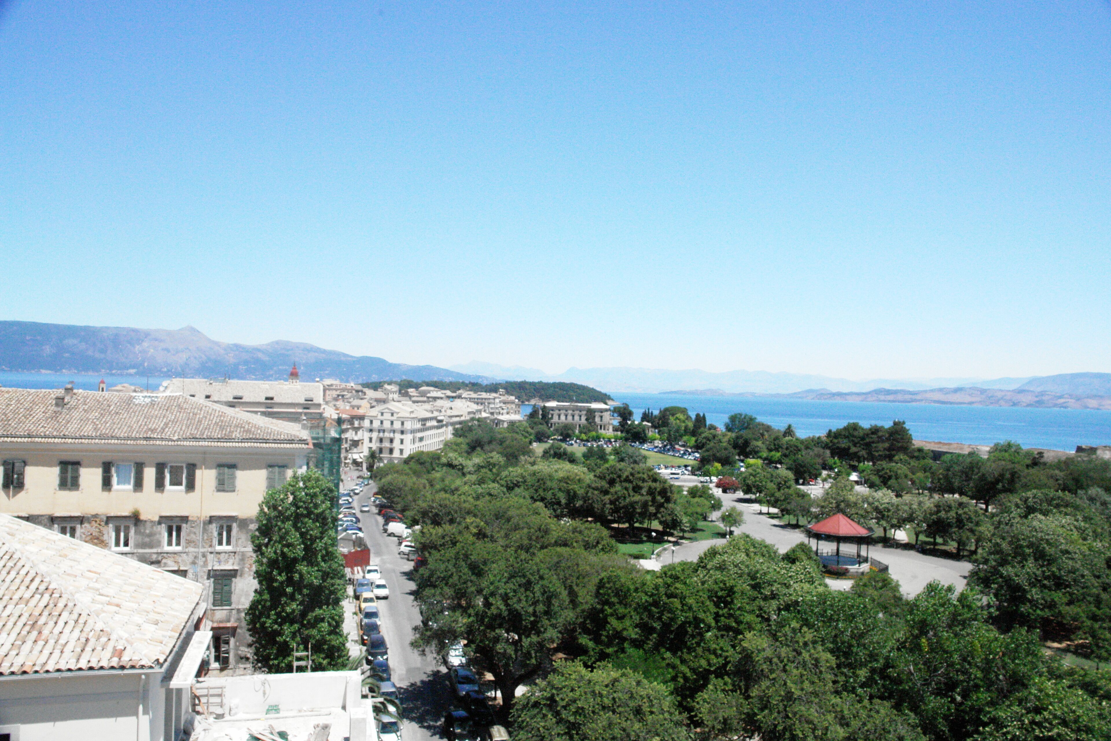 A coastal cityscape with buildings, a park, and a view of the sea.