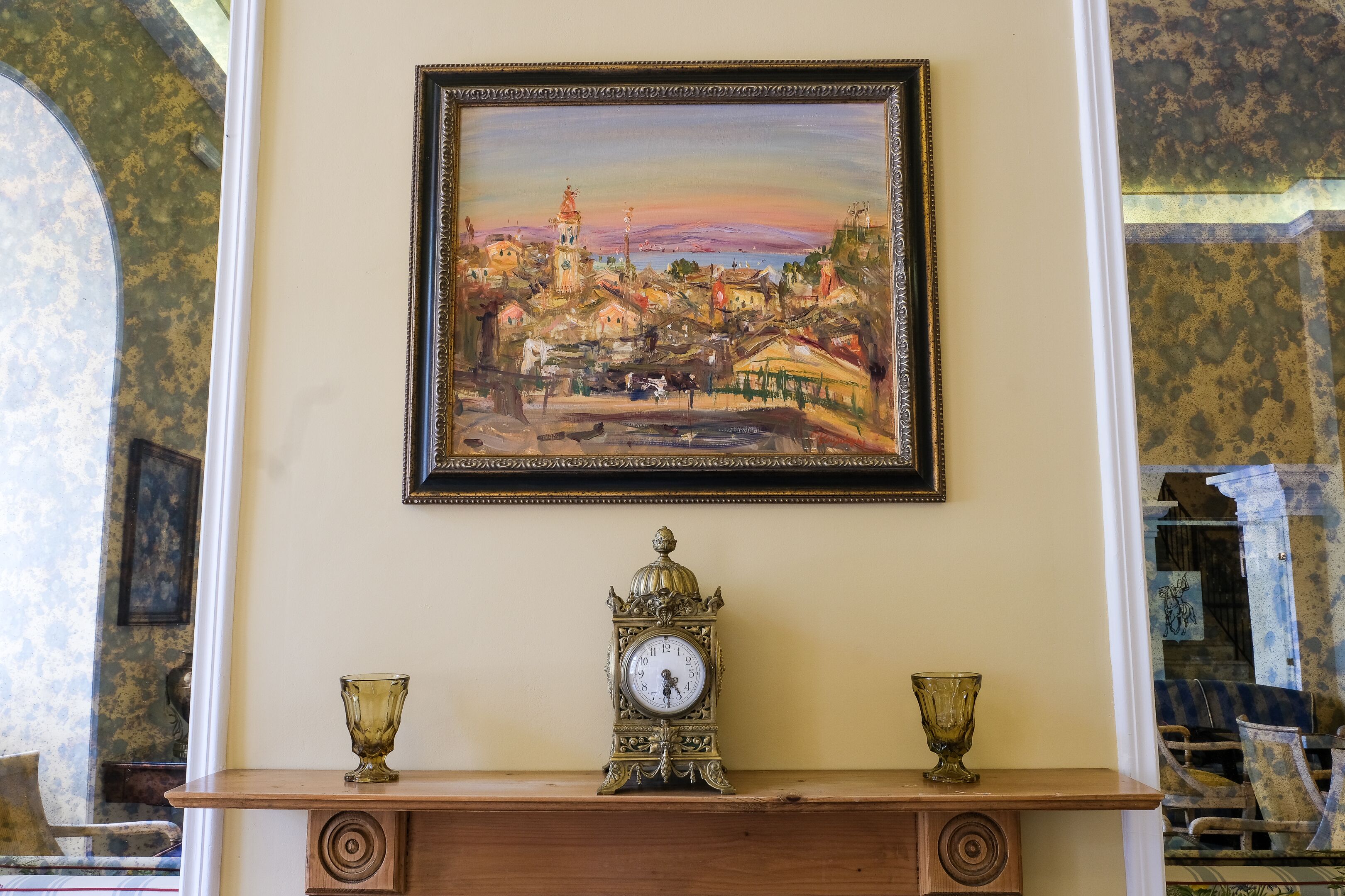 A framed painting of a cityscape, a vintage clock, and two decorative vases on a mantelpiece.