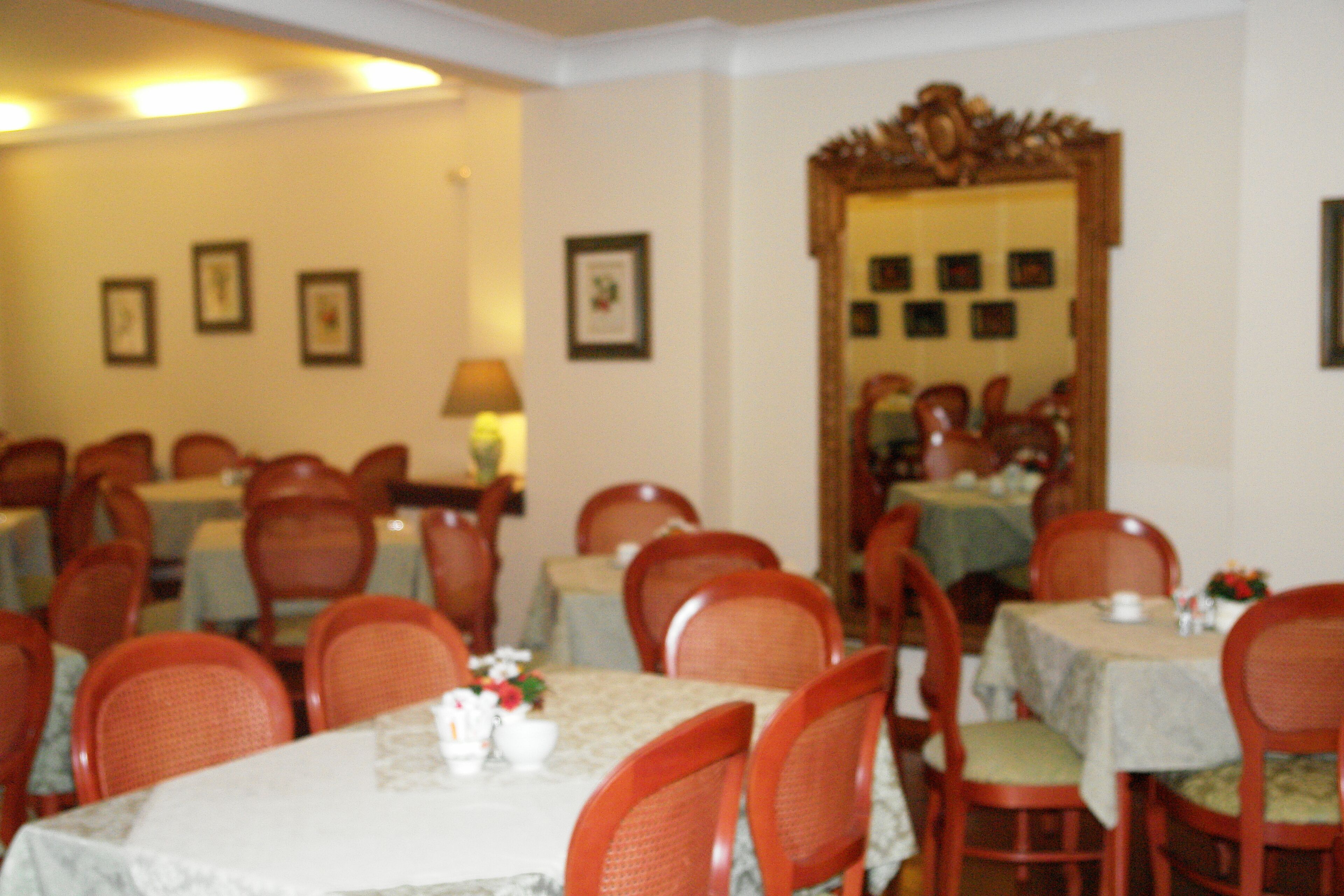 Un comedor con varias mesas y sillas, cuadros en las paredes y un espejo que refleja la estancia.