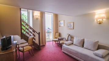 Habitación de hotel con alfombra de lunares rojos, un sofá, un televisor, un escritorio, una silla, una escalera y un balcón con vistas.