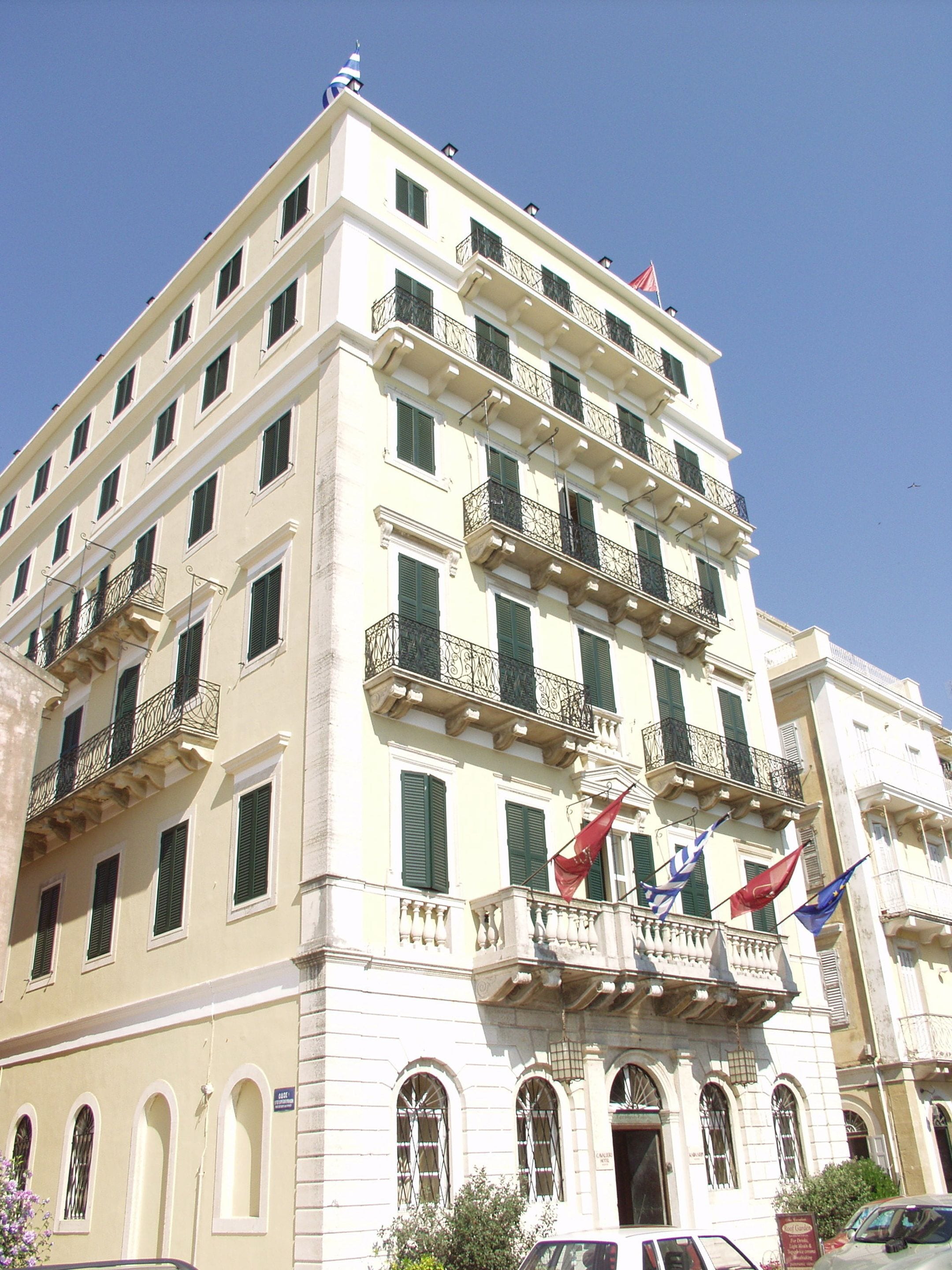A multi-story building with balconies, arched windows, and flags.
