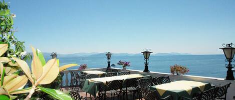 An outdoor patio with tables and chairs, overlooking a body of water and mountains.