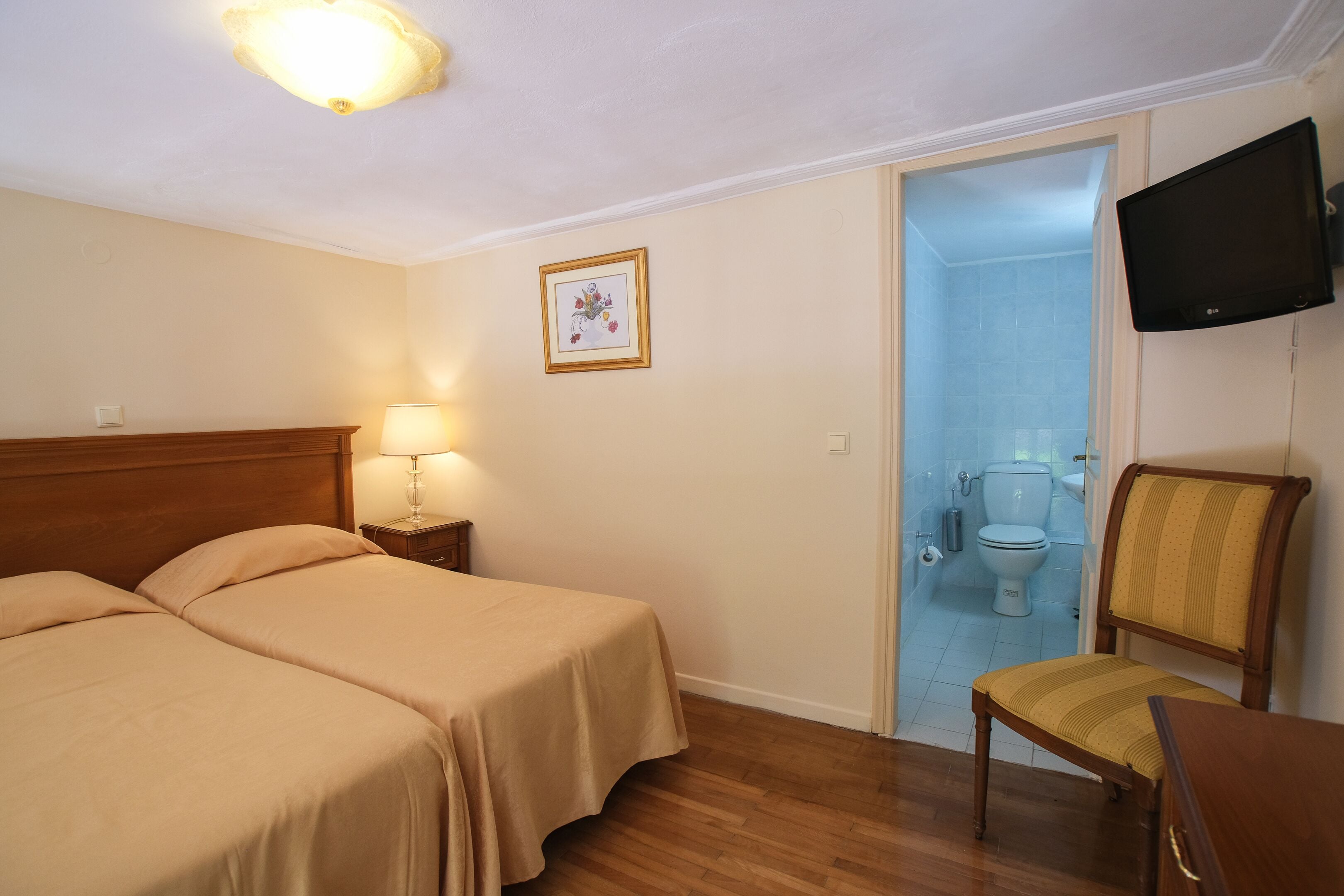 A hotel room with two beds, a chair, a TV, and a bathroom visible through an open door.