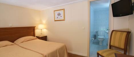 Quarto de hotel com duas camas, uma cadeira, televisão e banheiro visível por uma porta aberta.