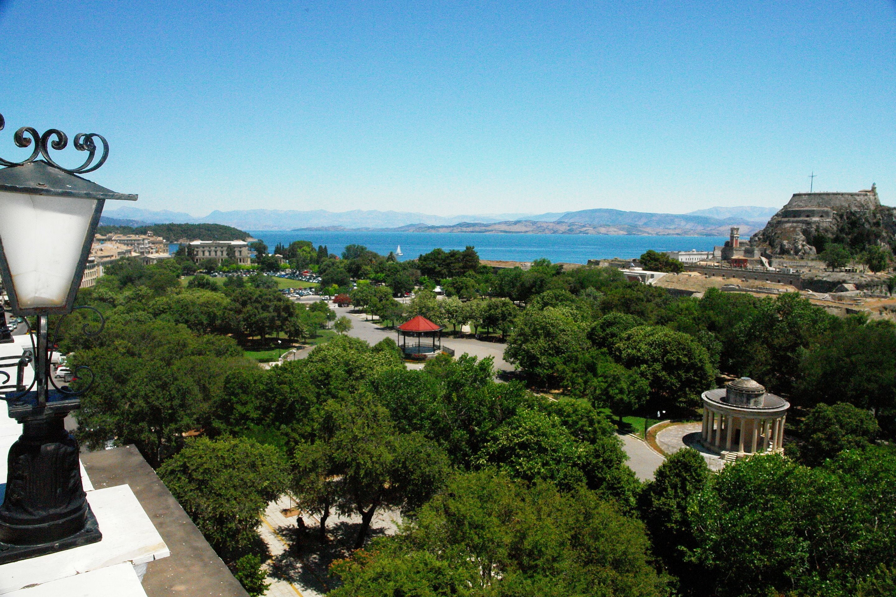 Um parque com um coreto, um edifício circular e uma vista distante de montanhas e água.