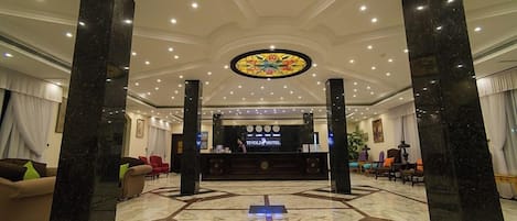 A hotel lobby with a reception desk, black marble pillars, and a patterned floor.